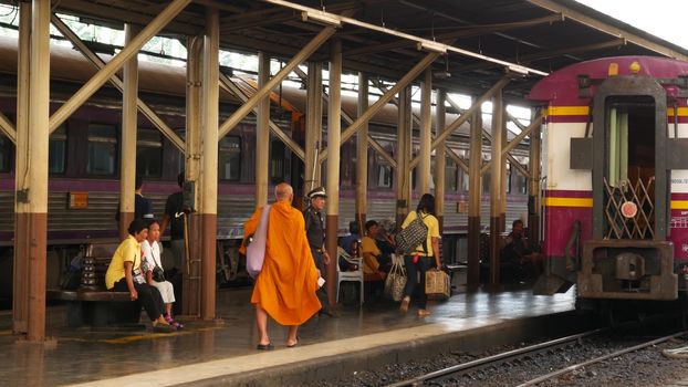 BANGKOK, THAILAND - 11 JULY 2019: Hua Lamphong railroad station, state railway transport infrastructure SRT. Buddhist holy Monk in traditional orange robe. Monks yellow religious clothes among people