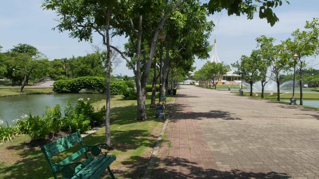 BANGKOK, THAILAND - 12 JULY, 2019: Blooming garden near pavilion in park. Green trees and flowers growing near pavilion building against cloudless blue sky on sunny day in King Rama IX Park