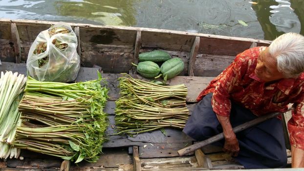 BANGKOK, THAILAND - 13 JULY 2019: Lat Mayom floating market. Traditional classic khlong river canal, local women farmers, long-tail boats with fruits and vegetables. Iconic asian street food selling