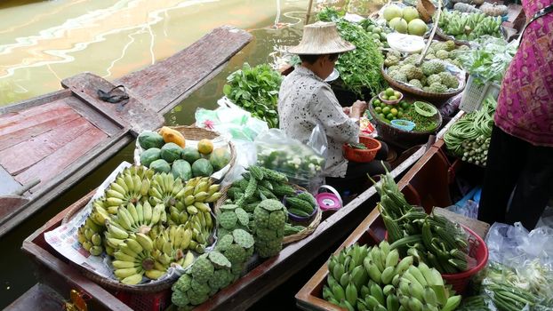 BANGKOK, THAILAND - 13 JULY 2019: Lat Mayom floating market. Traditional classic khlong river canal, local women farmers, long-tail boats with fruits and vegetables. Iconic asian street food selling