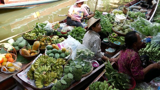 BANGKOK, THAILAND - 13 JULY 2019: Lat Mayom floating market. Traditional classic khlong river canal, local women farmers, long-tail boats with fruits and vegetables. Iconic asian street food selling