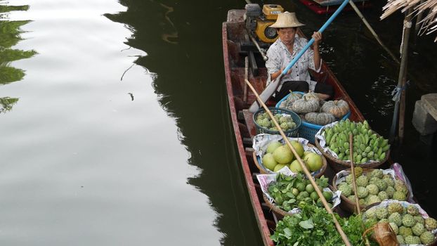 BANGKOK, THAILAND - 13 JULY 2019: Lat Mayom floating market. Traditional classic khlong river canal, local women farmers, long-tail boats with fruits and vegetables. Iconic asian street food selling