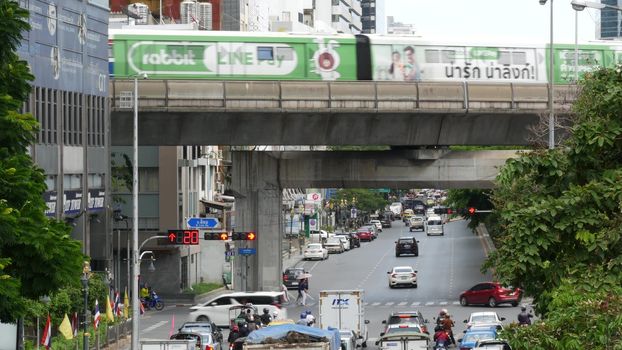BANGKOK, THAILAND - 13 JULY, 2019: Traffic on modern city street. Contemporary train riding on railroad bridge over road with cars in center of capital