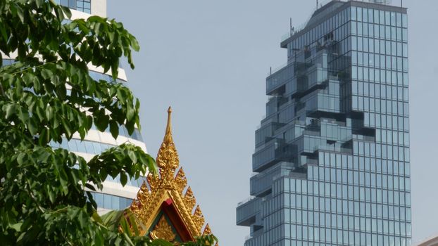 BANGKOK, THAILAND - 13 JULY, 2019: Conceptual contrast of oriental old traditional ancient temple and modern new futuristic Mahanakhon skyscraper. Classic buddhist wat compared to urban cityscape