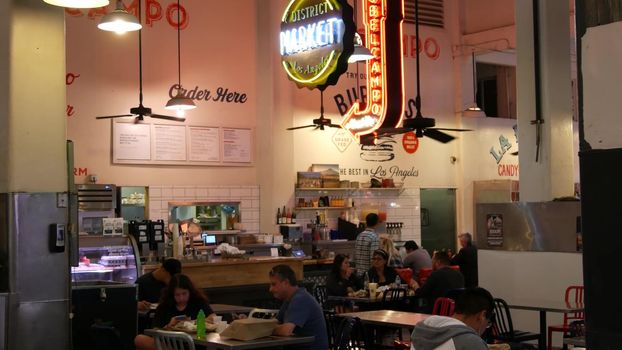 LOS ANGELES, CALIFORNIA, USA - 30 OCT 2019: Grand central market street lunch shops with diversity of glowing retro neon signs. Multiracial people on foodcourt. Citizens dining with fast food in LA.