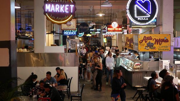 LOS ANGELES, CALIFORNIA, USA - 27 OCT 2019: Grand central market street lunch shops with diversity of glowing retro neon signs. Multiracial people on foodcourt. Citizens dining with fast food in LA.