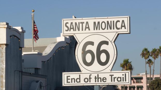 SANTA MONICA, LOS ANGELES, USA - 28 OCT 2019: Historic route 66, famous vintage california trip symbol. Pier of pacific ocean resort. Iconic retro road sign against the blue sky in amusement park.