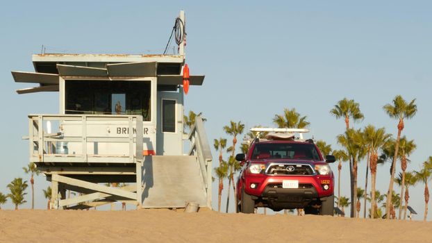 LOS ANGELES CA USA - 16 NOV 2019: California summertime Venice beach aesthetic. Iconic retro wooden lifeguard watchtower, baywatch red car. Life buoy, american state flag and palms near Santa Monica.