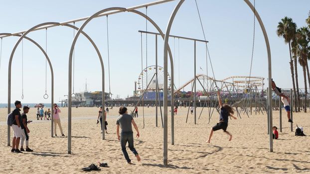 SANTA MONICA, LOS ANGELES CA USA - 28 OCT 2019: California summertime pacific ocean beach aesthetic, young people training and having fun on sports ground. Muscle beach and amusement park on pier.