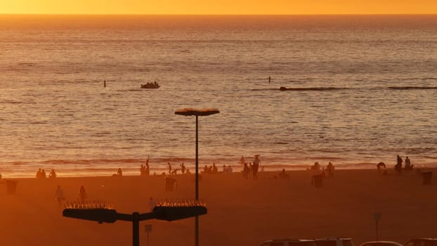 SANTA MONICA, LOS ANGELES, USA - 28 OCT 2019: California summertime beach aesthetic, atmospheric golden sunset. Unrecognizable people silhouettes, sun rays over pacific ocean waves.