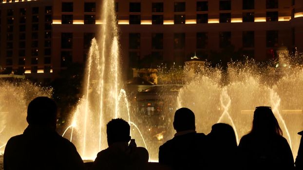 LAS VEGAS, NEVADA USA - 13 DEC 2019: People looking at Bellagio fountain musical performance at night. Contrast silhouettes and glowing dancing splashing water. Entertainment show in gambling city.