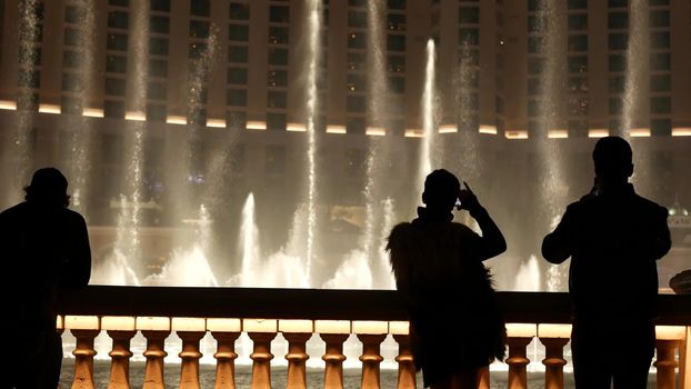 LAS VEGAS, NEVADA USA - 13 DEC 2019: People looking at Bellagio fountain musical performance at night. Contrast silhouettes and glowing dancing splashing water. Entertainment show in gambling city.