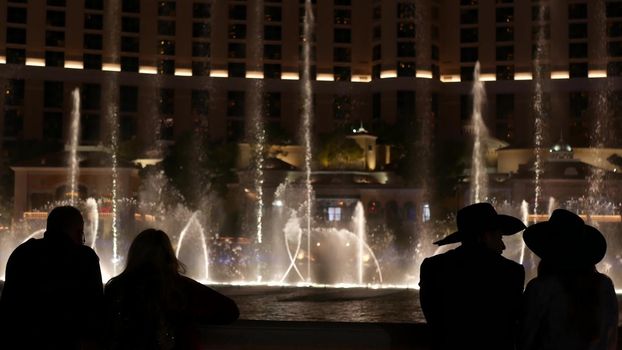 LAS VEGAS, NEVADA USA - 13 DEC 2019: People looking at Bellagio fountain musical performance at night. Contrast silhouettes and glowing dancing splashing water. Entertainment show in gambling city.