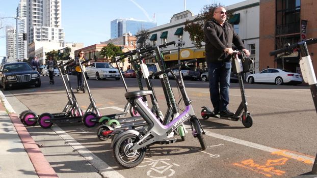 SAN DIEGO, CALIFORNIA USA - 4 JAN 2020: Row of ride sharing electric scooters parked on street in Gaslamp Quarter. Rental dockless public bikes, eco transport in city. Rent kick cycle with mobile app.