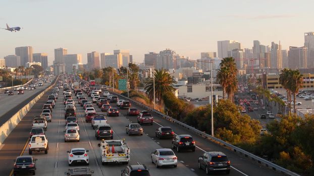 SAN DIEGO, CALIFORNIA USA - 15 JAN 2020: Busy intercity freeway, traffic jam on highway during rush hour. Urban skyline, highrise skyscraper and landing plane. Flying airplane, transportation concept.