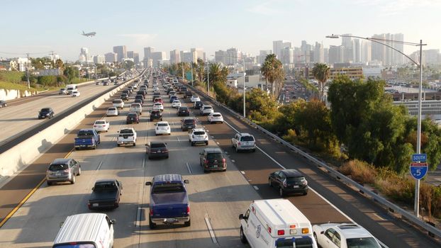 SAN DIEGO, CALIFORNIA USA - 15 JAN 2020: Busy intercity freeway, traffic jam on highway during rush hour. Urban skyline, highrise skyscraper and landing plane. Flying airplane, transportation concept.