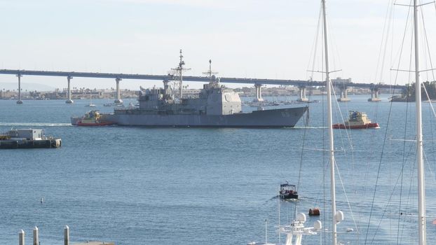 SAN DIEGO, CALIFORNIA USA - 13 FEB 2020: Tugboat pulling USS Chosin CG-65, military warship of US Navy fleet. Tug towing maritime battleship in port harbor. United States Armed Forces naval ship.