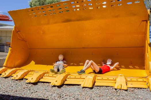 2 young people taking a nap in a mining front loader bucket for scale.