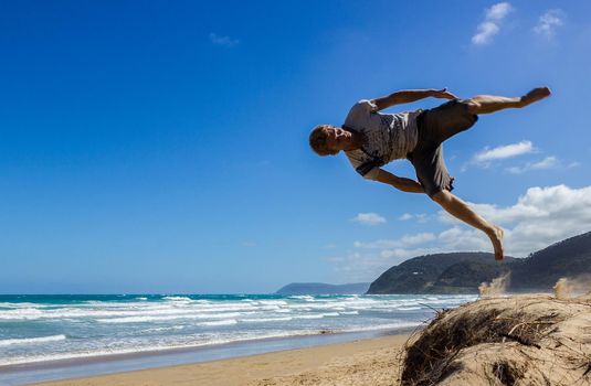Portrait of young parkour man doing flip or somersault on the sand.