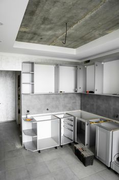 Custom kitchen cabinets installation without a furniture facades mdf. Gray modular kitchen from chipboard material on a various stages of installation in kitchen with a grey tile on floor and walls