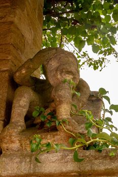 An old stone sculpture on the top of a wall surrounded by plants