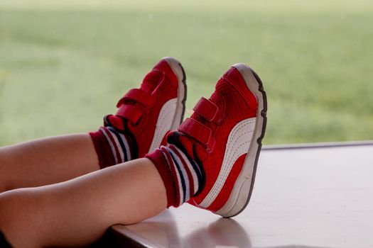 Close-up of two baby feet on red trainers on a wood table