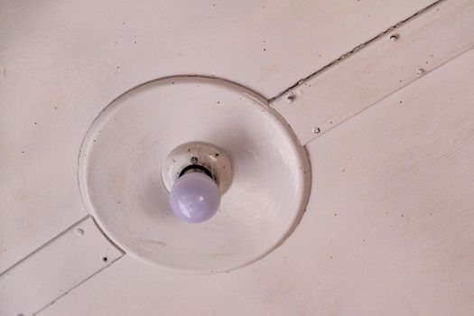 A white lamp with a white lightbulb on a white ceiling