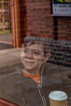 Portrait of a blue-eyed, red-haired, four years old boy looking through a train window holding a paper cup