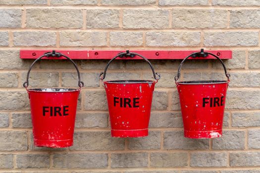 Three red metal fire buckets hanging on a stone wall