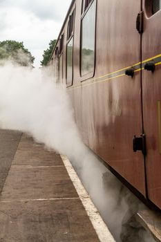 An old passenger train carriage surrounded by a steam cloud in a countryside station