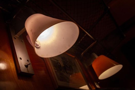 Two lamps with lampshades hanging on a wooden wall in a dark room