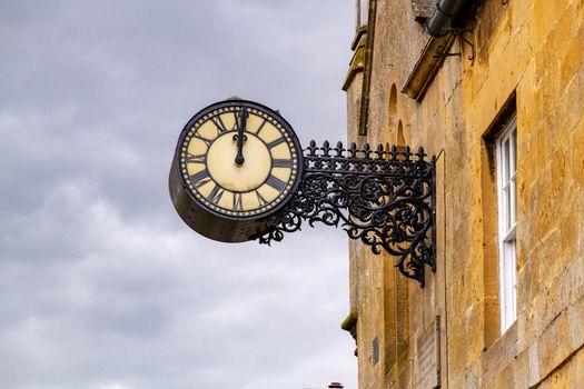 An old iron clock hanging on a stone wall against a grey, cloudy sky