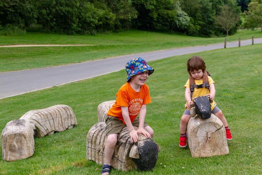 A cute red-haired, four years old boy and a baby girl playing on a lawn with some wooden sheep.