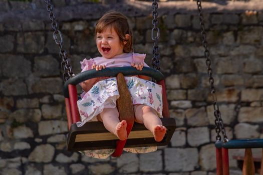 A cute, blue-eyed, brown-haired, baby girl smiling in a swing on a sunny summer day