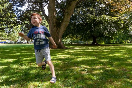 Full-length shot of one cute, blue-eyed, red-haired, four years old boy running in a park