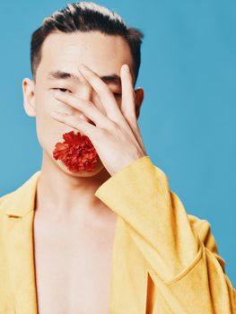 A man touches his face with his hand and a red flower in his mouth on a blue background. High quality photo