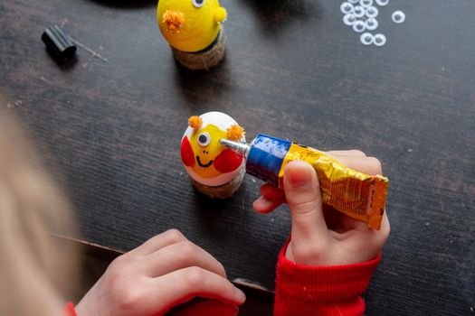 A girl decorates an egg for easter and glues funny eyes to it