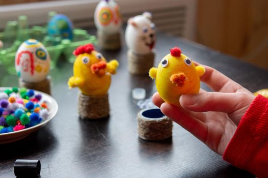 The child made a figurine of a chicken from an egg and shows it into the frame, in the background other figures