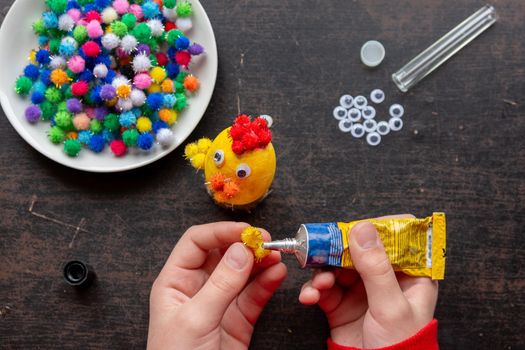 children's hands glue the wing to the chicken figure with glue from a tube