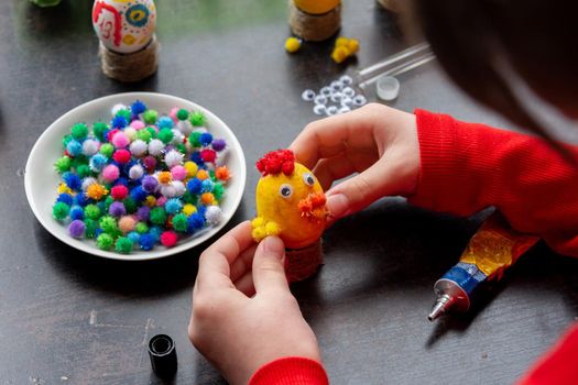 A girl glues wings to a chicken figurine made from an egg