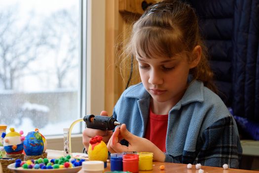 A girl glues a decorative element to crafts with a glue gun