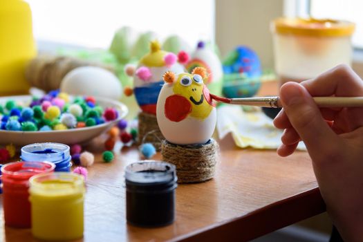 Child's hand draws a funny face on Easter egg