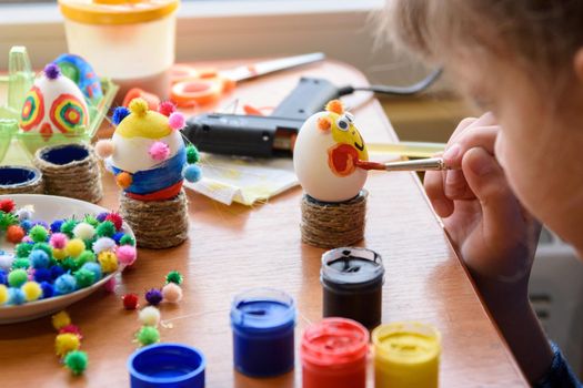 Girl carefully and neatly paints Easter eggs, close-up