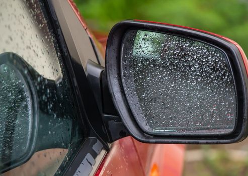 Closeup of car side rear view mirror with rain drops