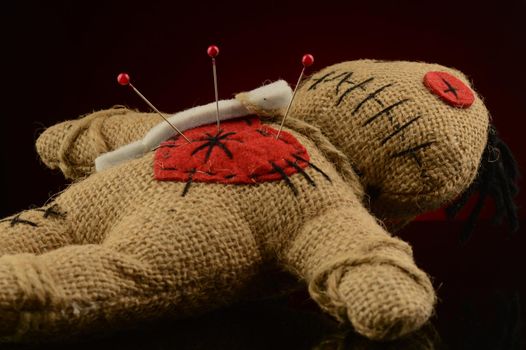 A few pins are stuck inside the heart of a voodoo doll over a dark red and black background.