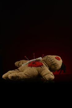 A few pins are stuck inside the heart of a voodoo doll over a dark red and black background.