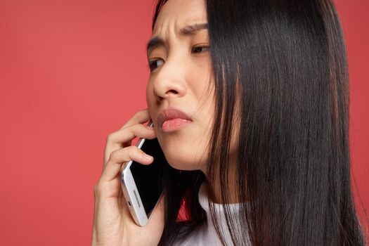 woman of asian appearance and contented facial expression talking on the phone close-up red fund. High quality photo