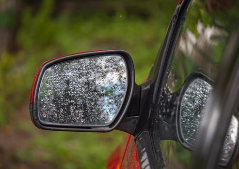 Closeup of car side rear view mirror with rain drops