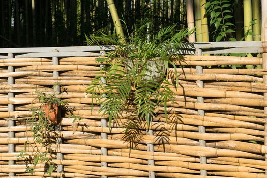 A fence of bamboo weave with hanging baskets with flowers