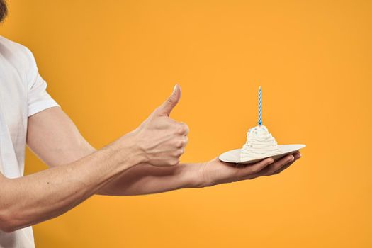 Cake with a candle in a man's hand on a yellow background cropped view Copy Space. High quality photo